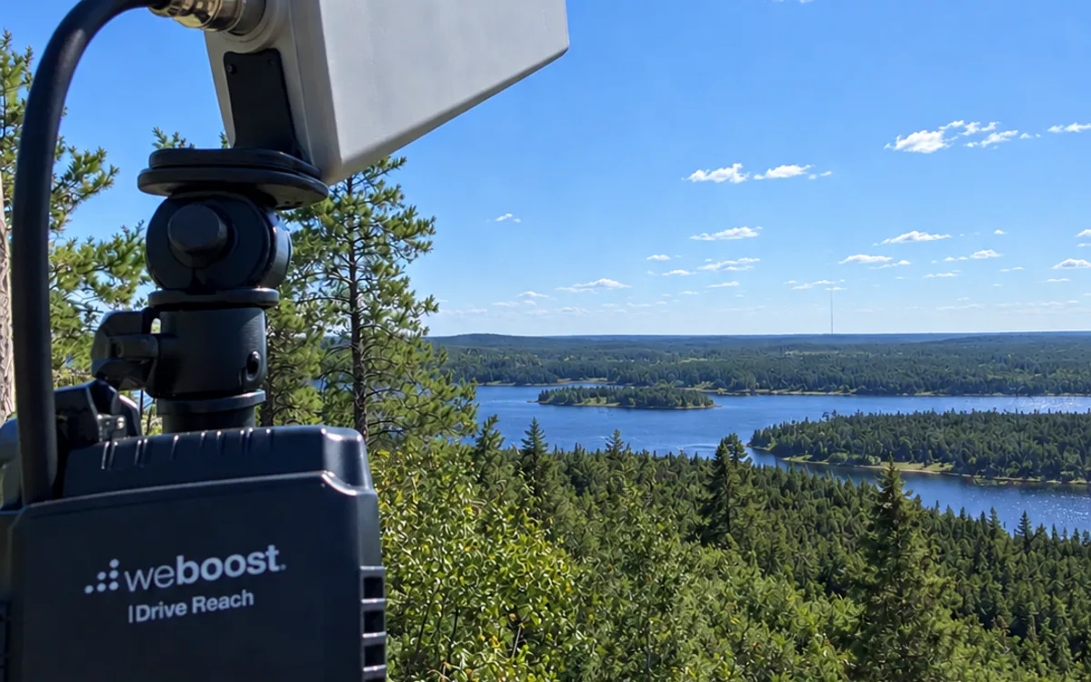 An outdoor booster antenna and weBoost unit overlooking a lake, with a cell tower on the horizon