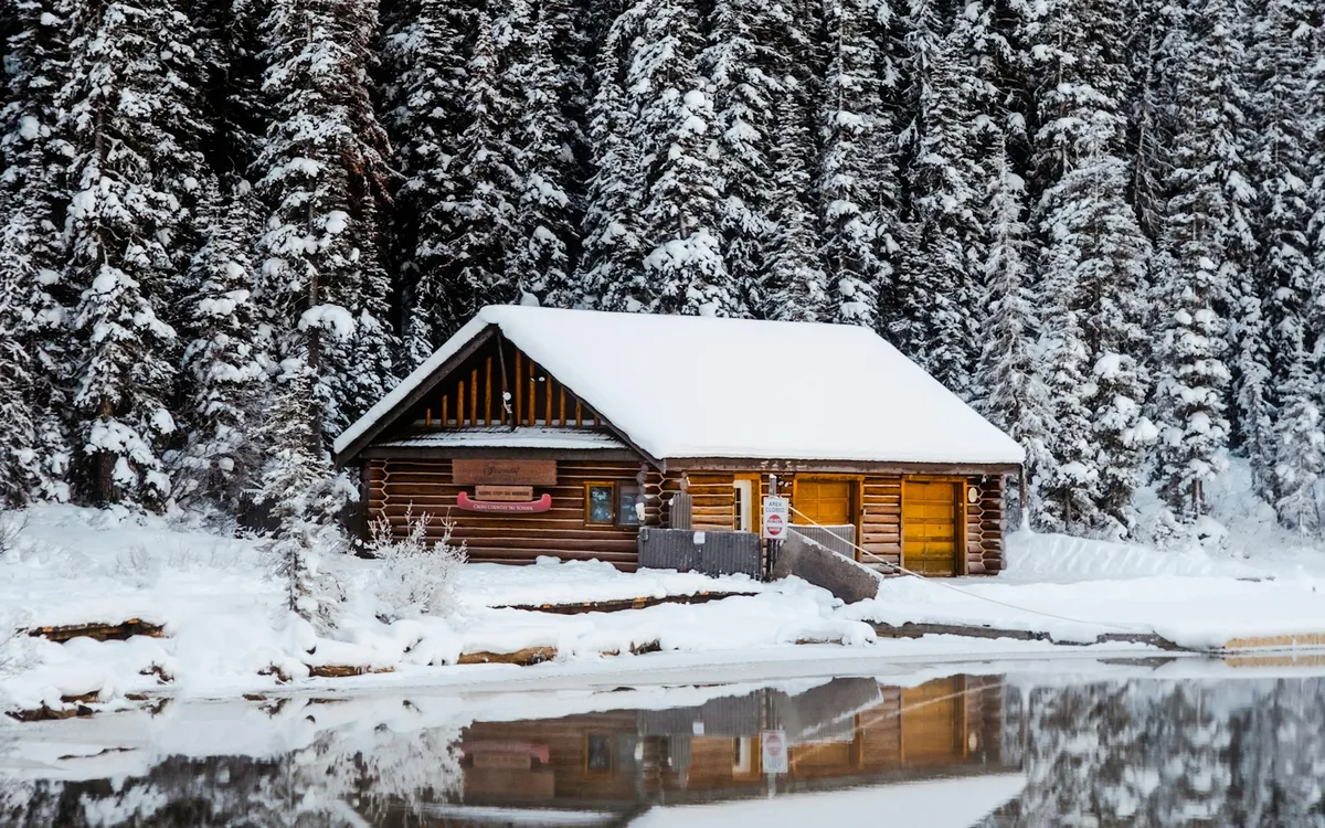A snow-covered log cabin beside a lake in winter